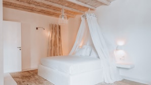 A bedroom with a bed, a bedside table, a nightstand, a wooden ceiling, and a wall-mounted light fixture. - Senses Villas (Mykonos)