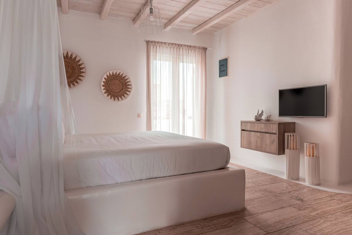 A bedroom with a bed, a TV, and a window with curtains.