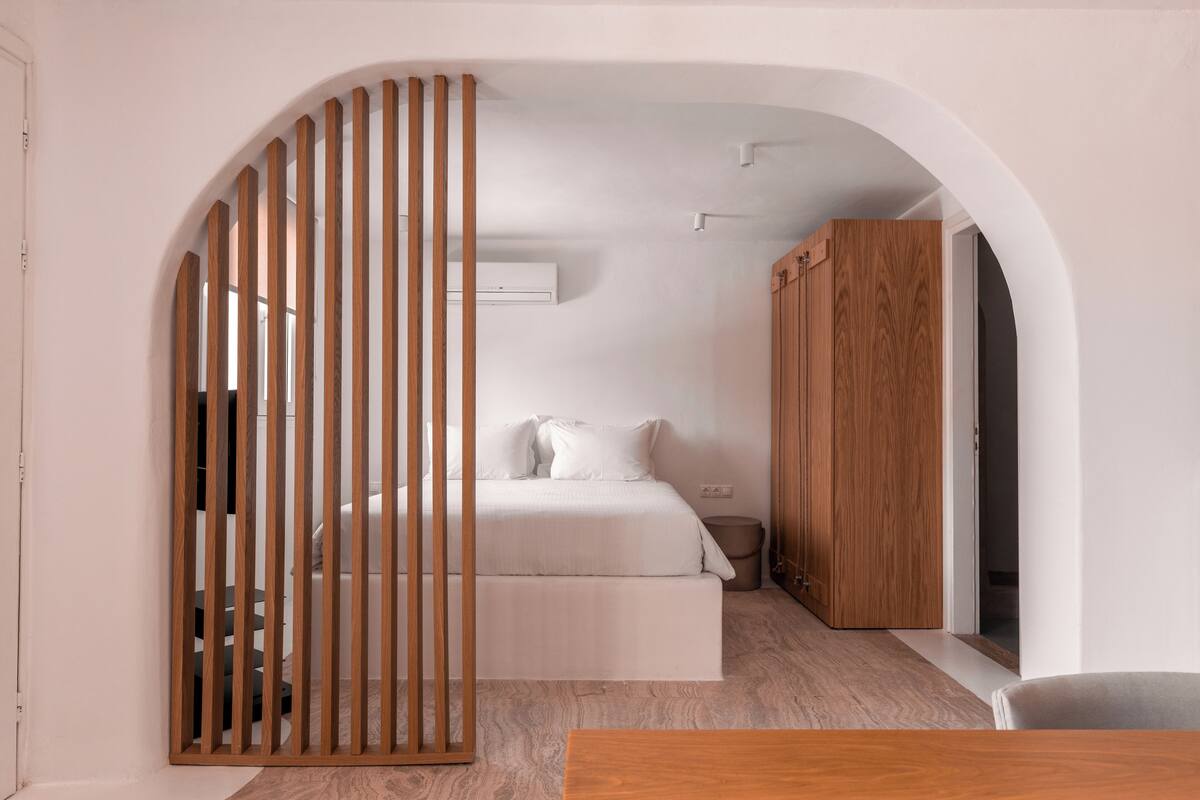 A bedroom with a bed, wooden wardrobe, and a partition with vertical slats.