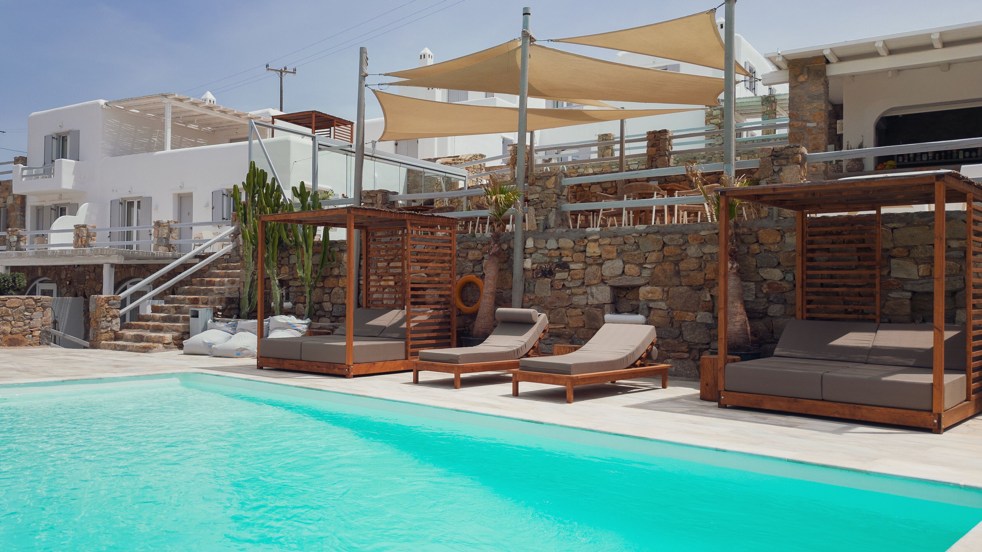 A poolside area with lounge chairs, a wooden pergola, and a stone wall.