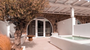 A spa area with a stone wall, a white infinity pool, and a glass door leading to a seating area. - Senses Villas (Mykonos)