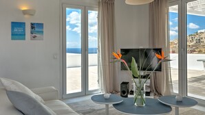 A modern living room with a sofa, a TV, and a view of the sea through large windows. - Senses Villas (Mykonos)