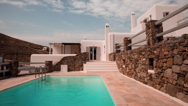 A modern white building with a stone wall and a swimming pool. - Senses Villas (Mykonos)
