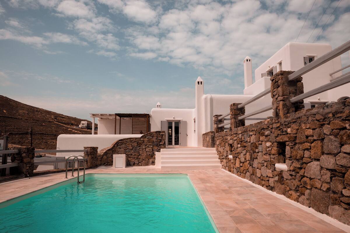 A modern white building with a stone wall and a swimming pool.