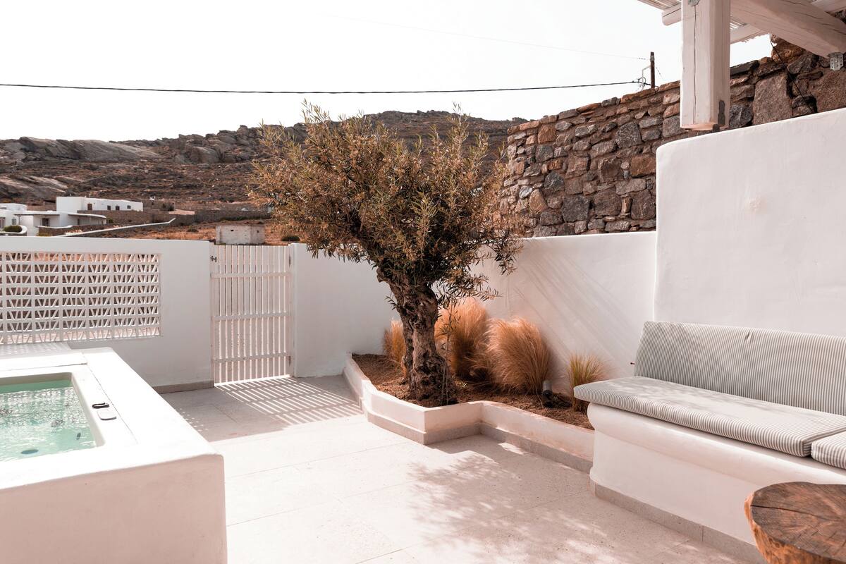 A modern outdoor patio with a white sofa, a small tree, and a hot tub.