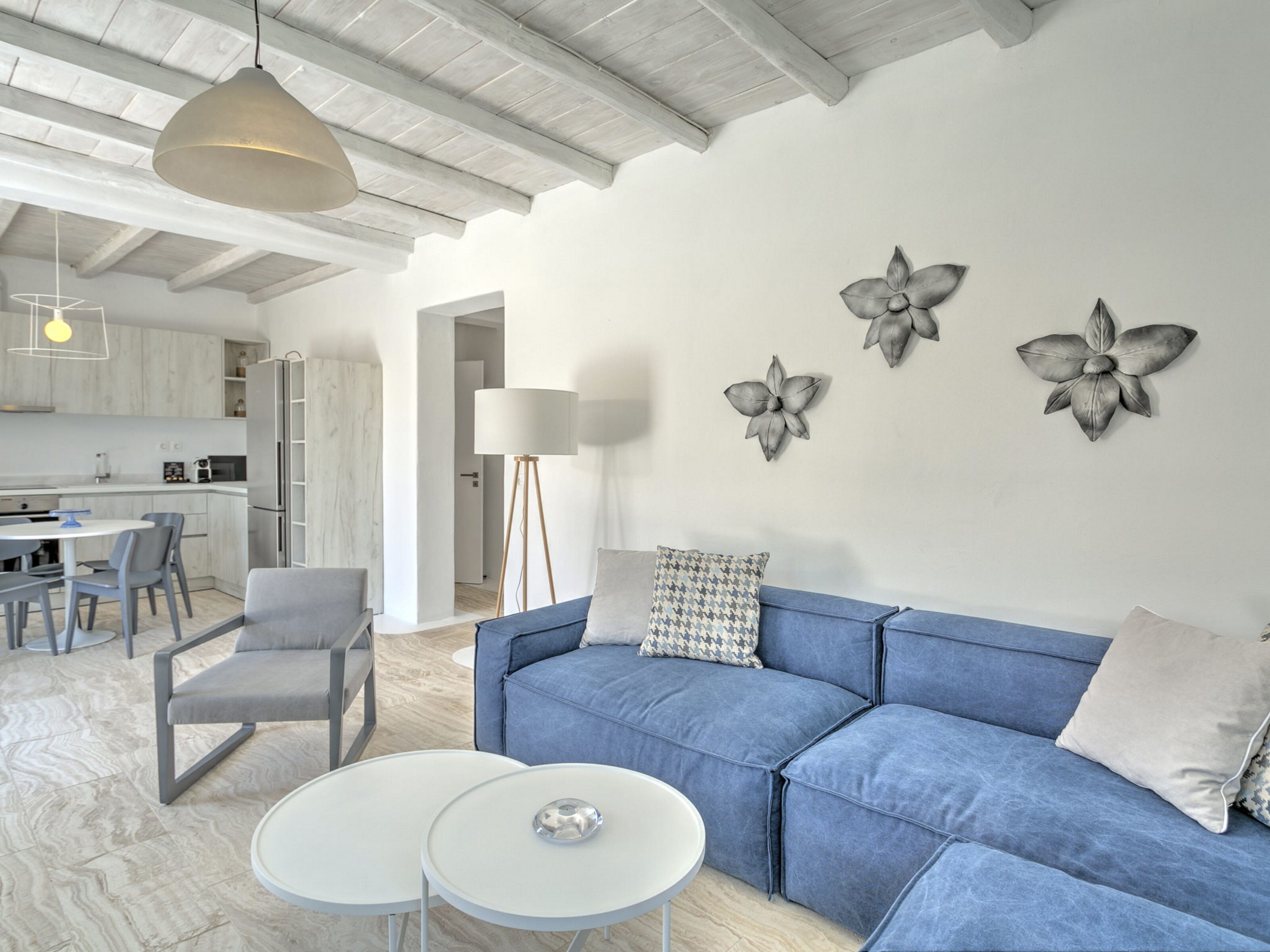 A modern living room with a blue sofa, two white round tables, and a kitchen in the background.
