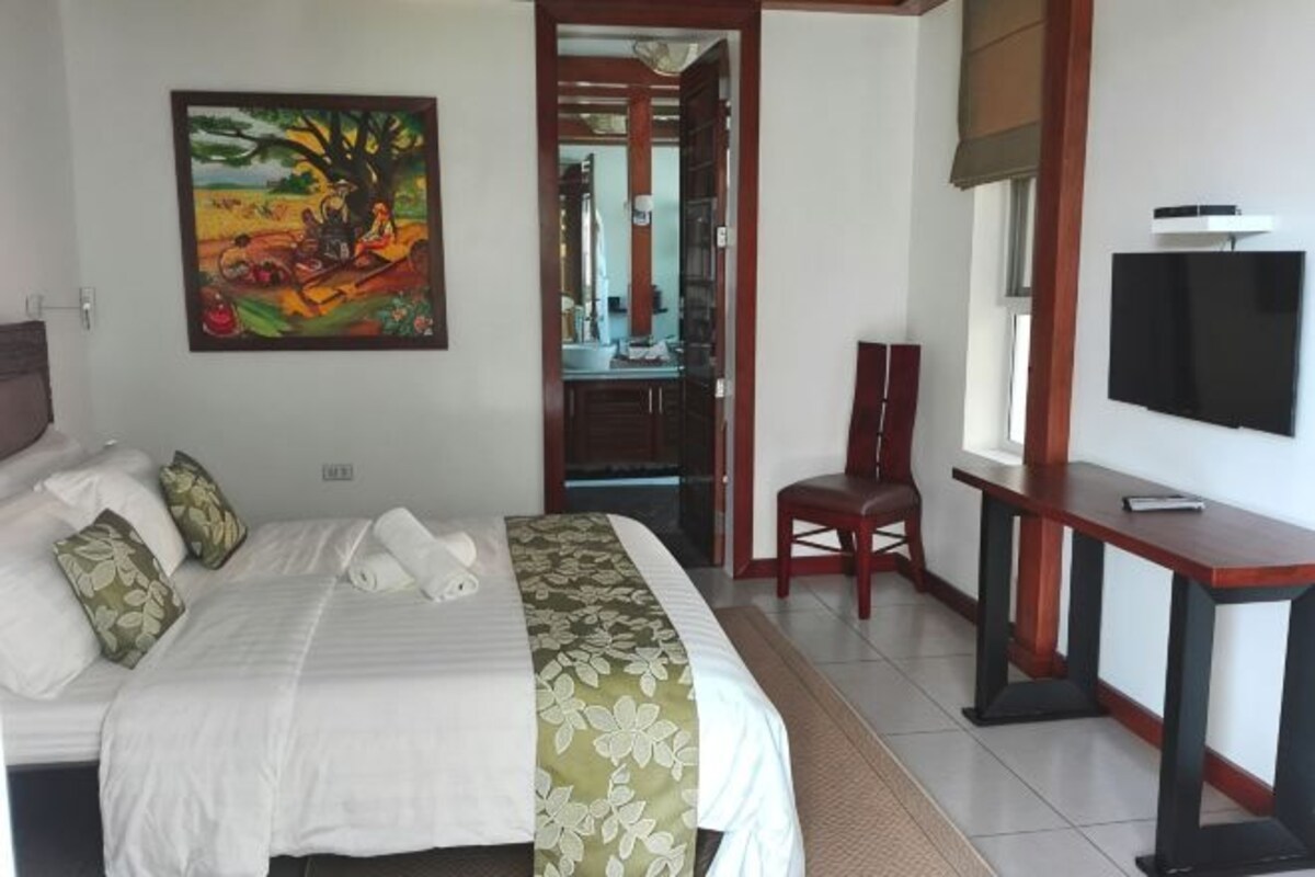 Habitación de hotel con cama, escritorio, silla, televisor y un cuadro en la pared.