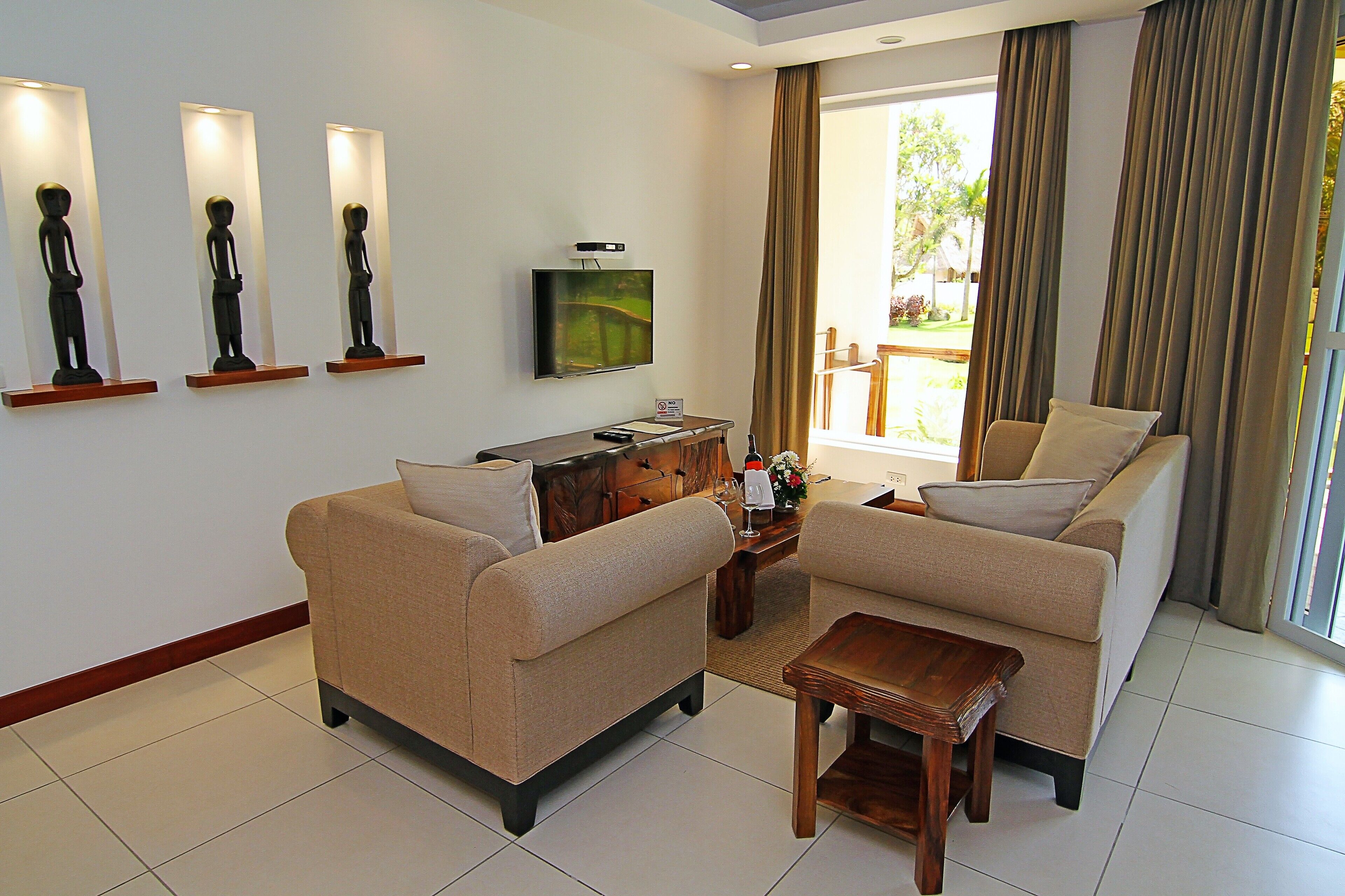 A modern living room with two beige sofas, a wooden coffee table, a flat-screen TV on a stand, and three wall-mounted sculptures.