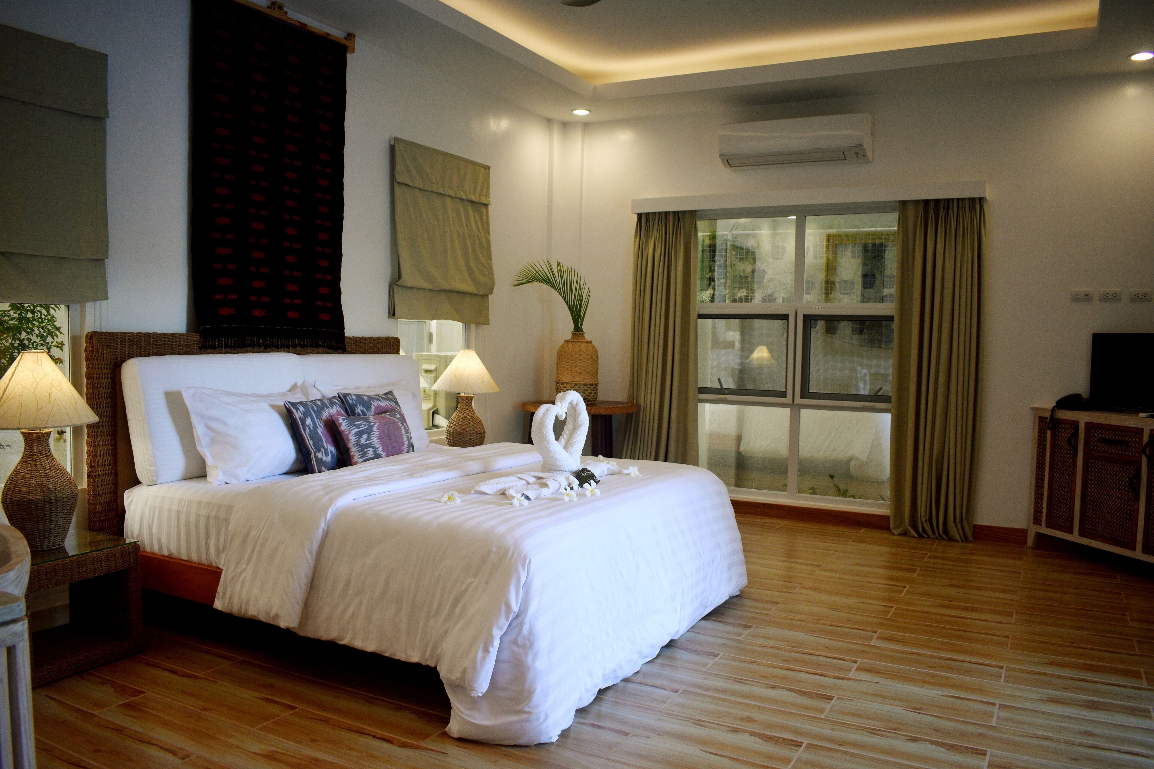 Une chambre d’hôtel avec un grand lit, une fenêtre avec des rideaux, une table de chevet avec une lampe et un téléviseur posé sur un meuble.