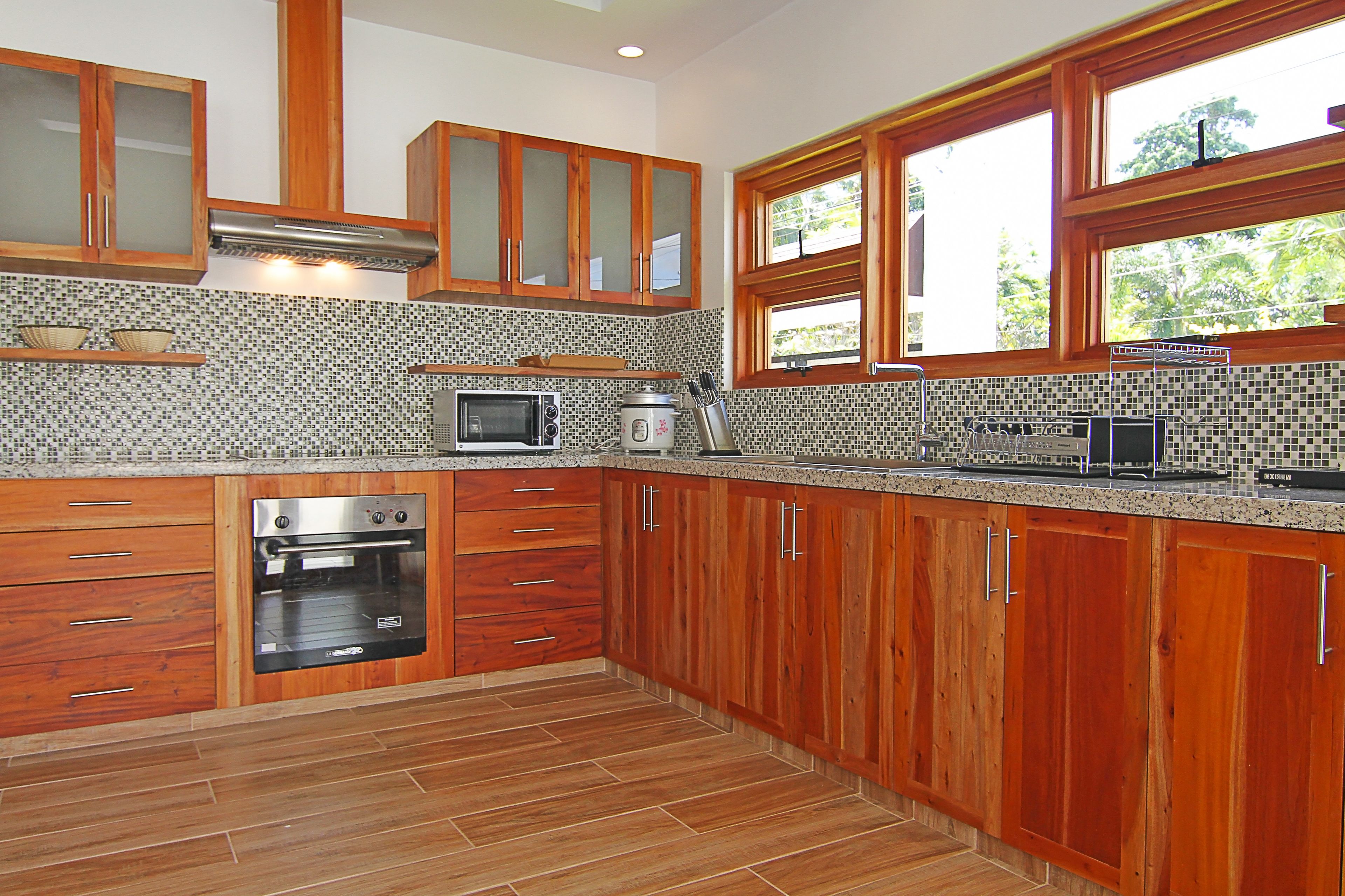 A kitchen with wooden cabinets, a built-in oven, a microwave, and a window with a view of greenery.