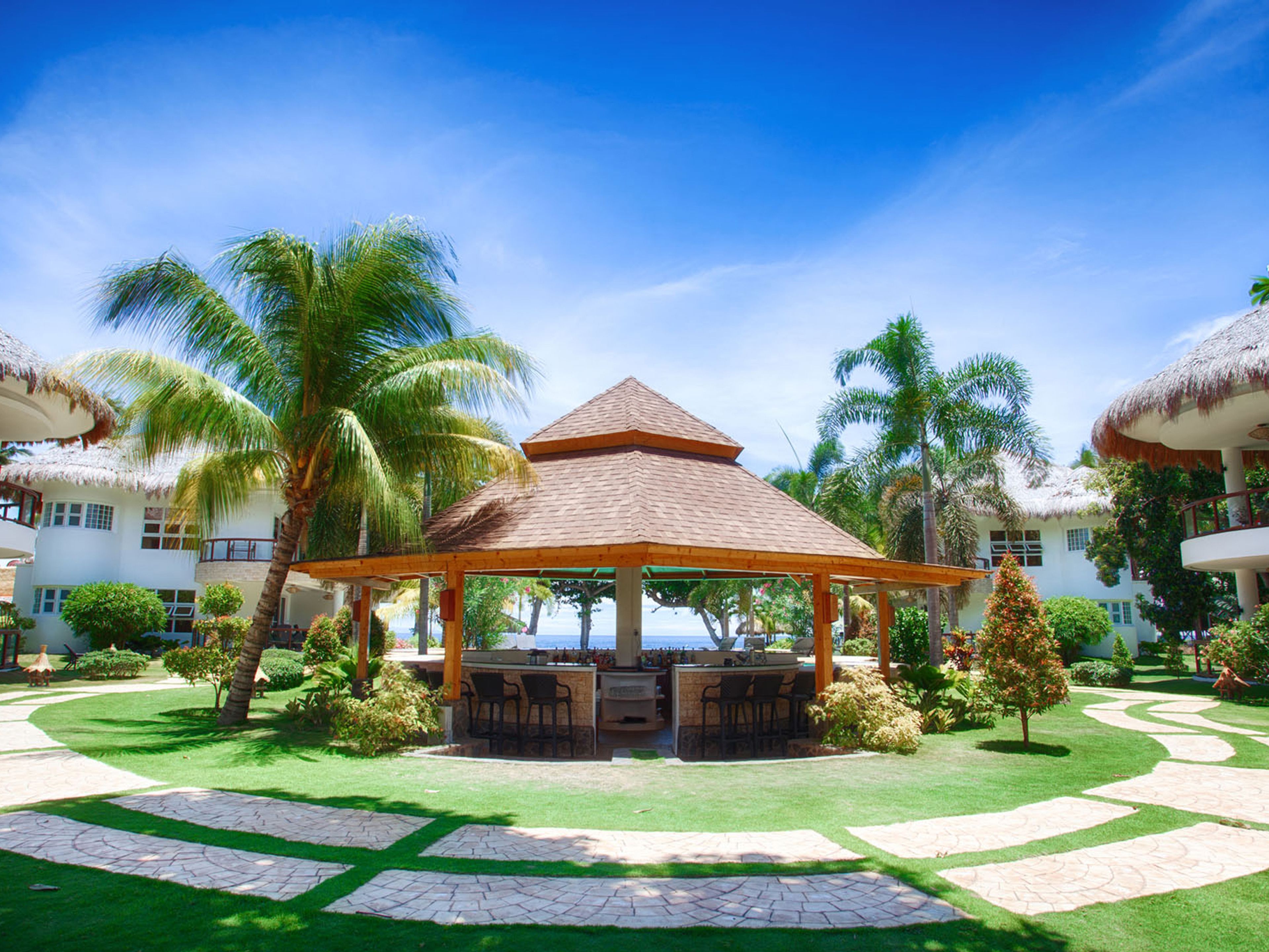 A resort with a central gazebo, palm trees, and a clear view of the ocean.