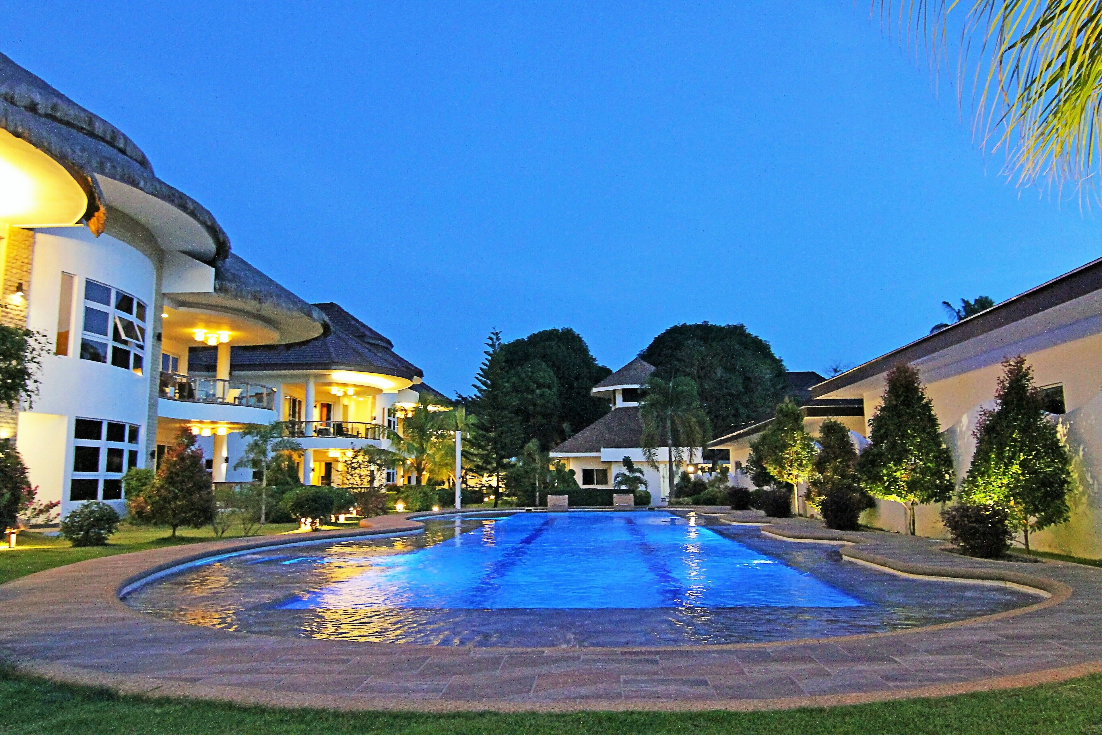 A swimming pool surrounded by a well-maintained lawn and a large building with multiple balconies and windows.