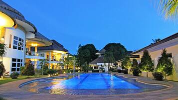 A swimming pool surrounded by a well-maintained lawn and a large building with multiple balconies and windows.