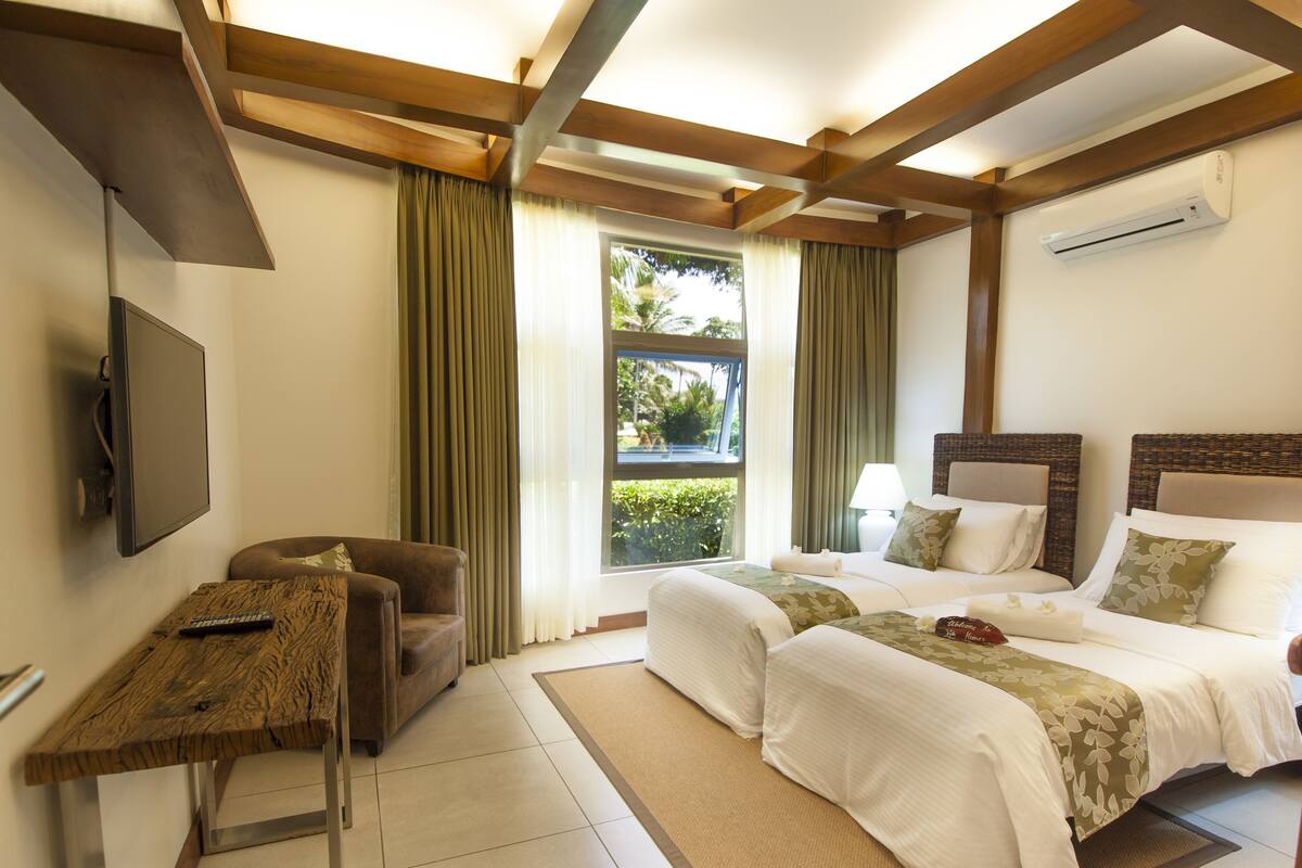 Une chambre d’hôtel avec un lit, un bureau, une chaise, une télévision et une fenêtre avec des rideaux.