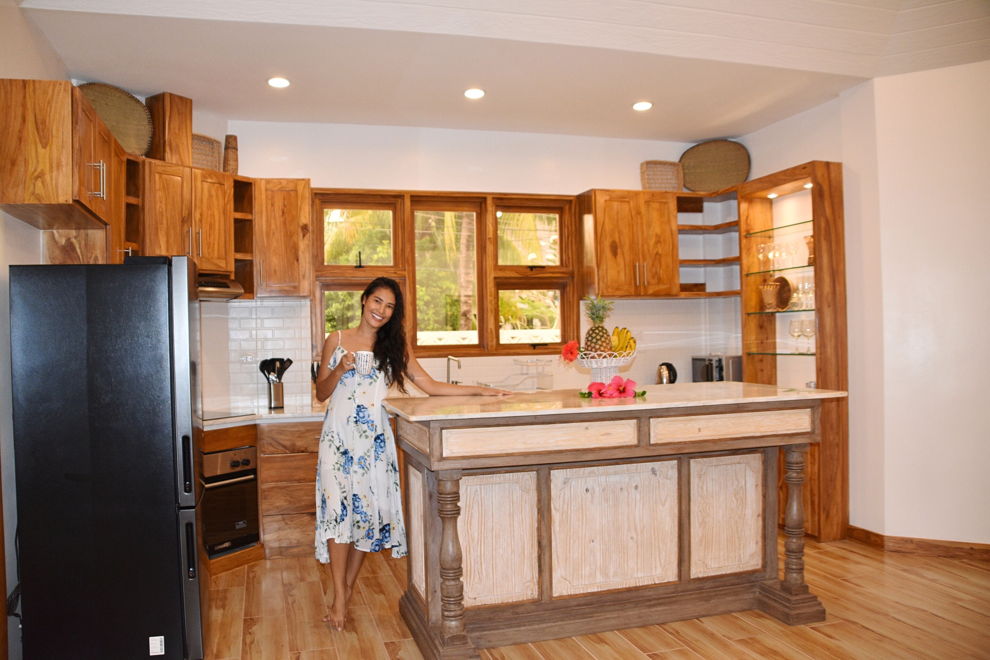 Cocina con armarios de madera, refrigerador negro, una isla central y una ventana con vista a la vegetación.