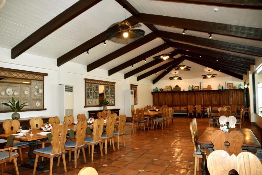 A spacious dining area with wooden tables and chairs, a high ceiling with exposed beams, and a tiled floor.