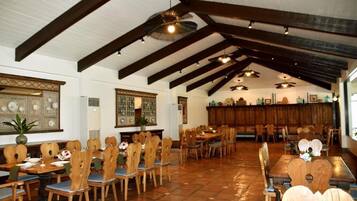 A spacious dining area with wooden tables and chairs, a high ceiling with exposed beams, and a tiled floor.