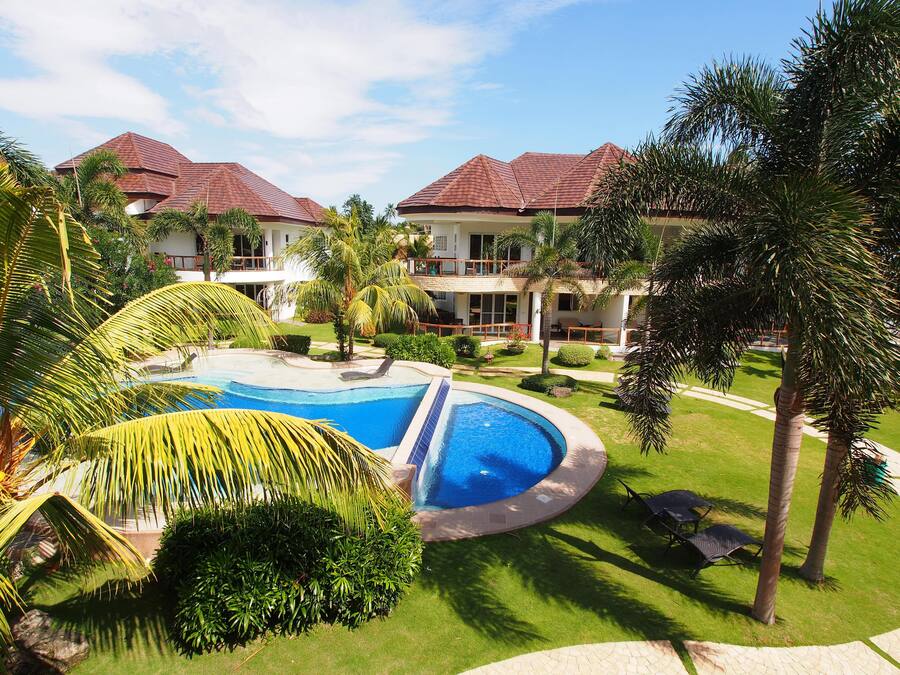 Resort com piscina, palmeiras e um edifício com telhado vermelho.