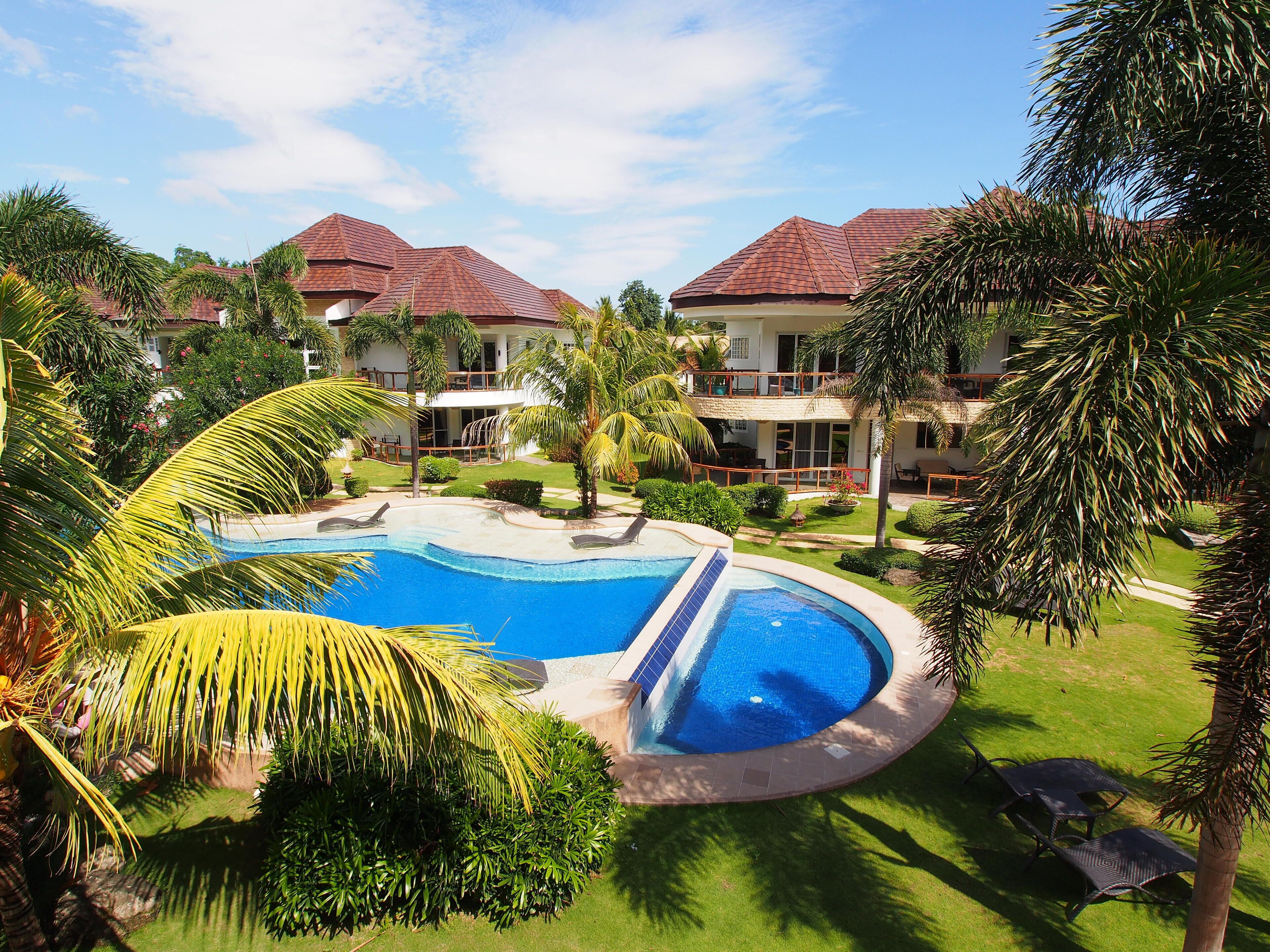 Un resort con piscina rodeada de palmeras y un césped cuidado.