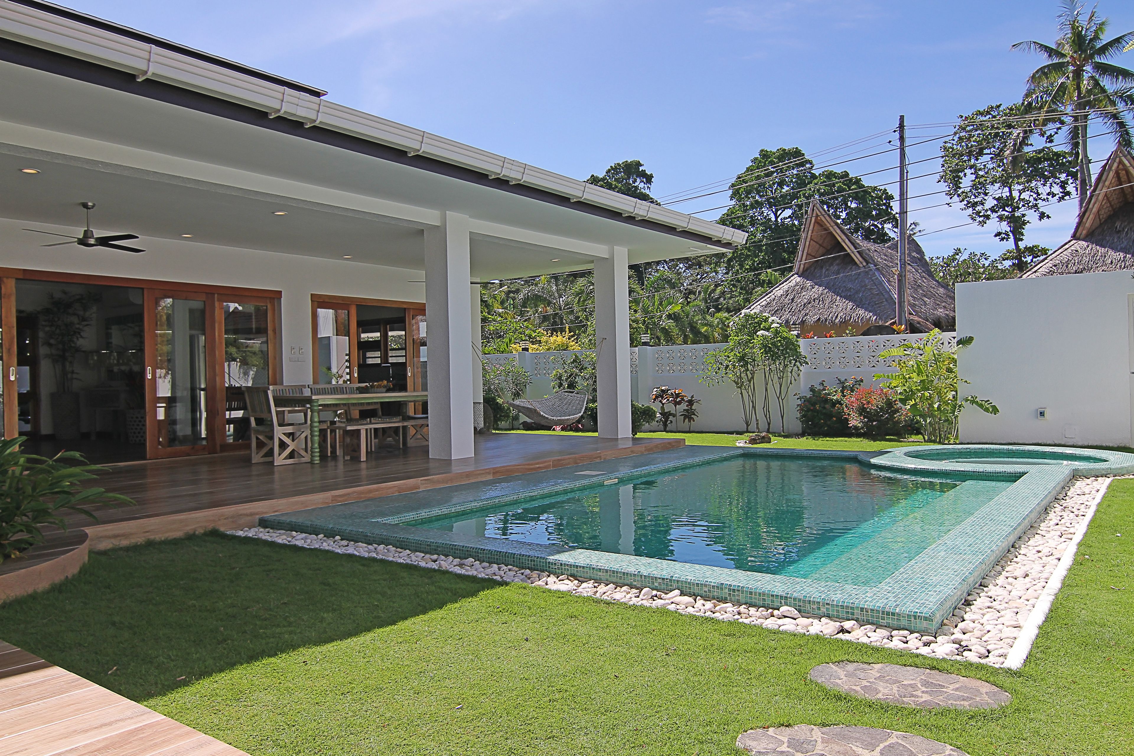 Una casa moderna con piscina, un patio cubierto y una estructura de techo de paja al fondo.