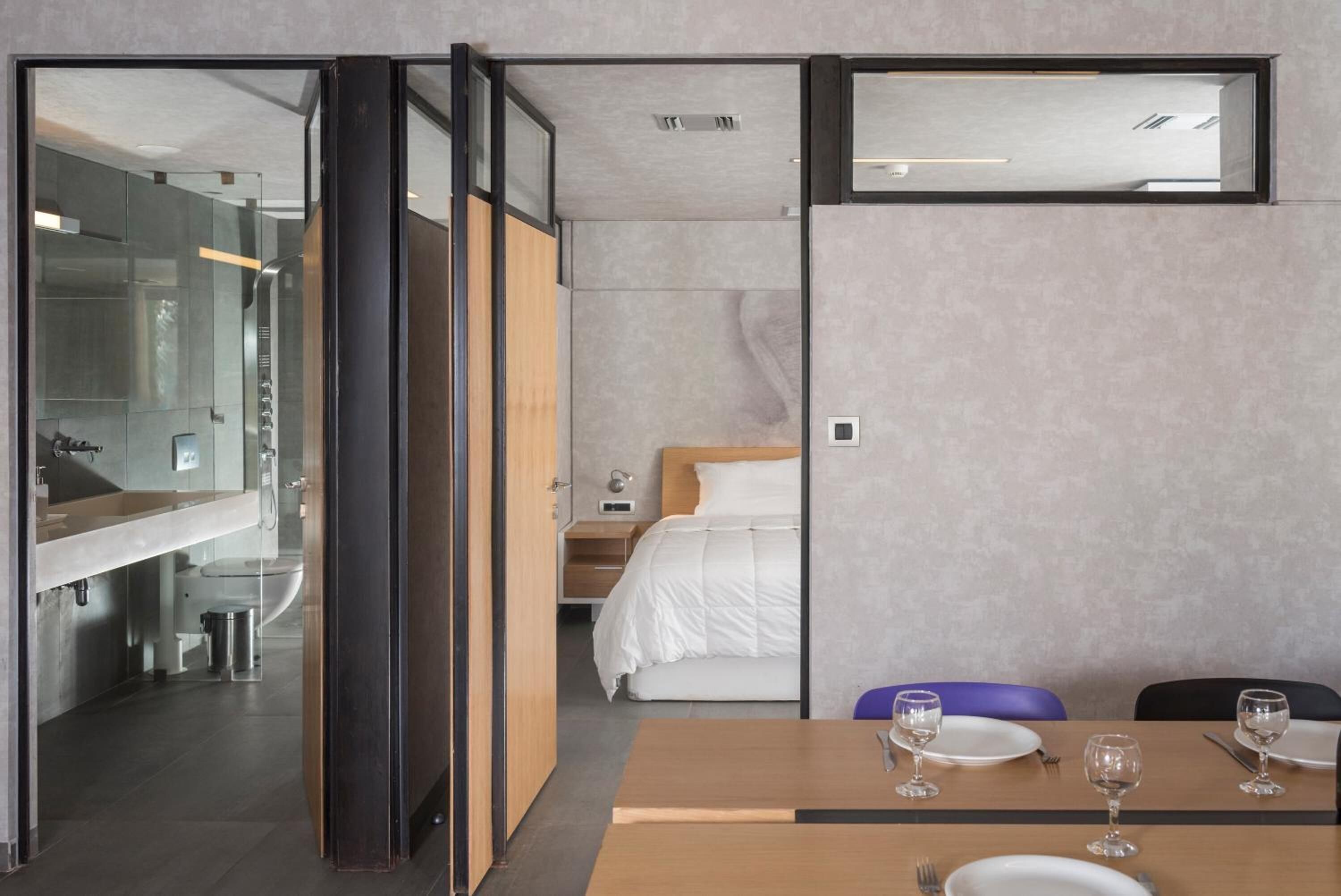 A modern hotel room with a wooden bed, a small bedside table, a nightstand, and a bathroom visible through an open door.