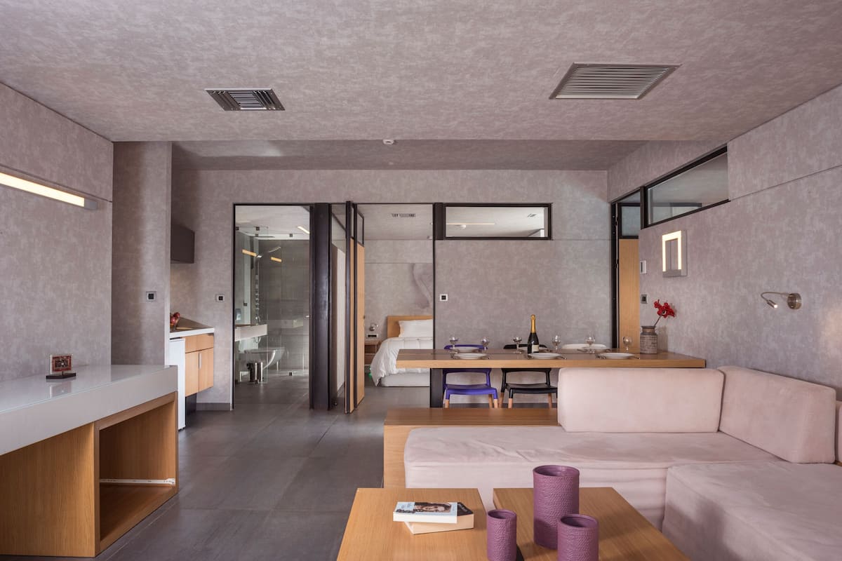 Una habitación de hotel moderna con kitchenette, un sofá, una mesa de comedor y un espejo grande.