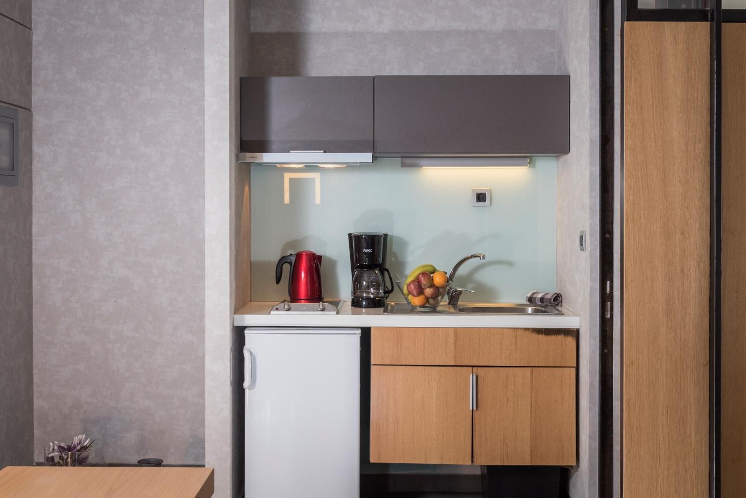 A compact kitchenette with a coffee maker, kettle, and fruit bowl on the counter.