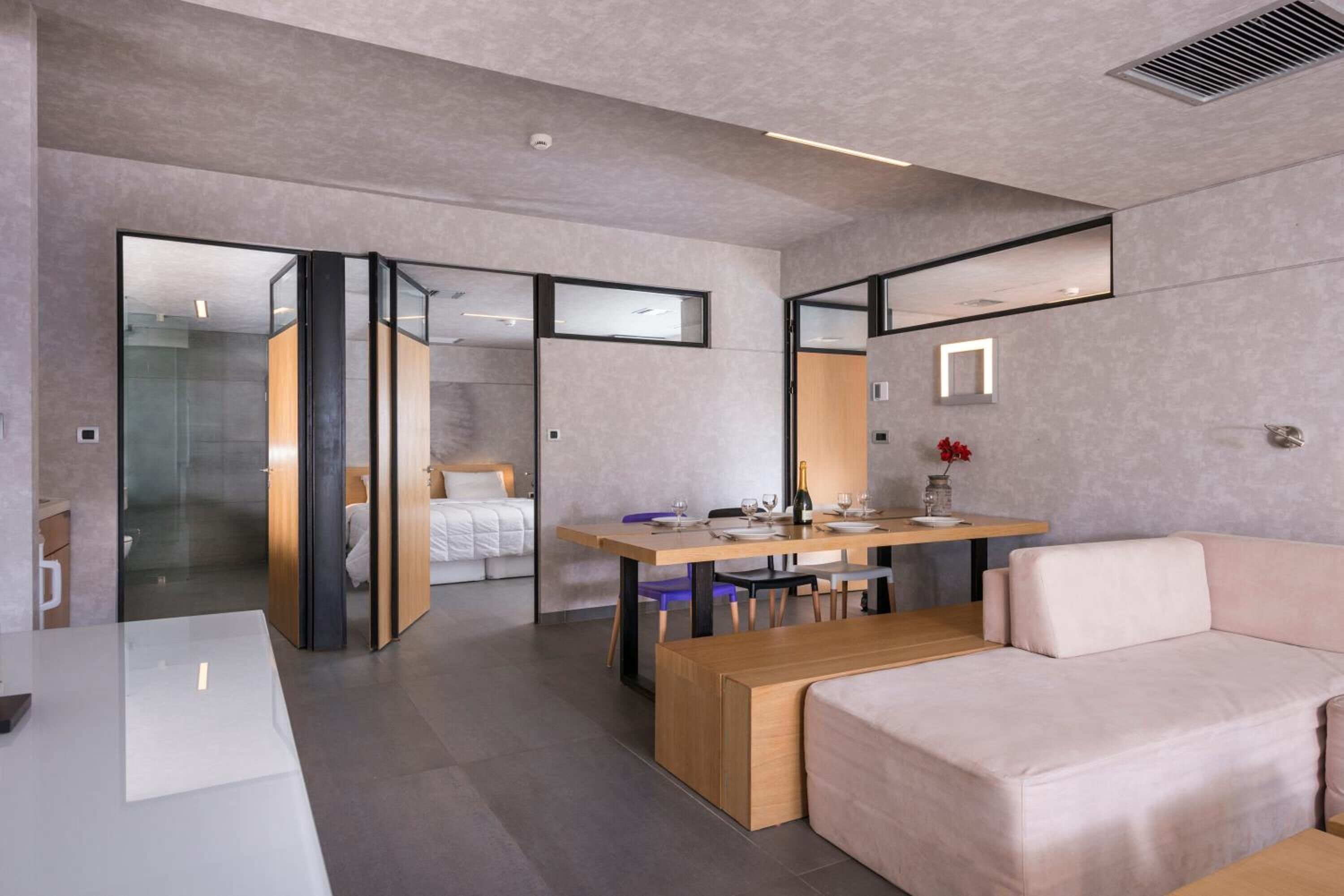 A modern hotel room with a glass partition separating the living area from the bedroom.