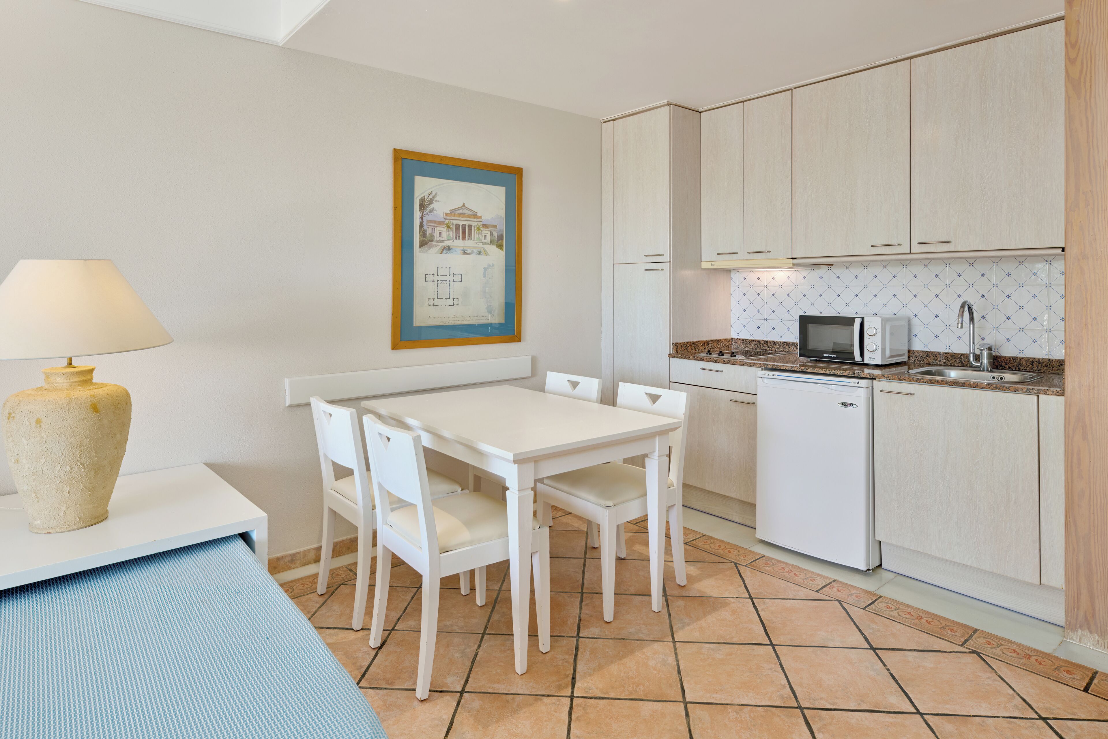 A compact kitchen with white cabinetry, a microwave, and a dining table with chairs.