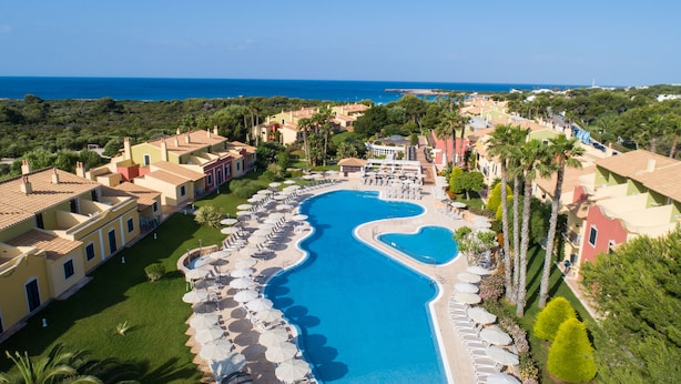 A resort with a large pool, multiple buildings, and a view of the sea. - Grupotel Playa Club (Ciutadella de Menorca)