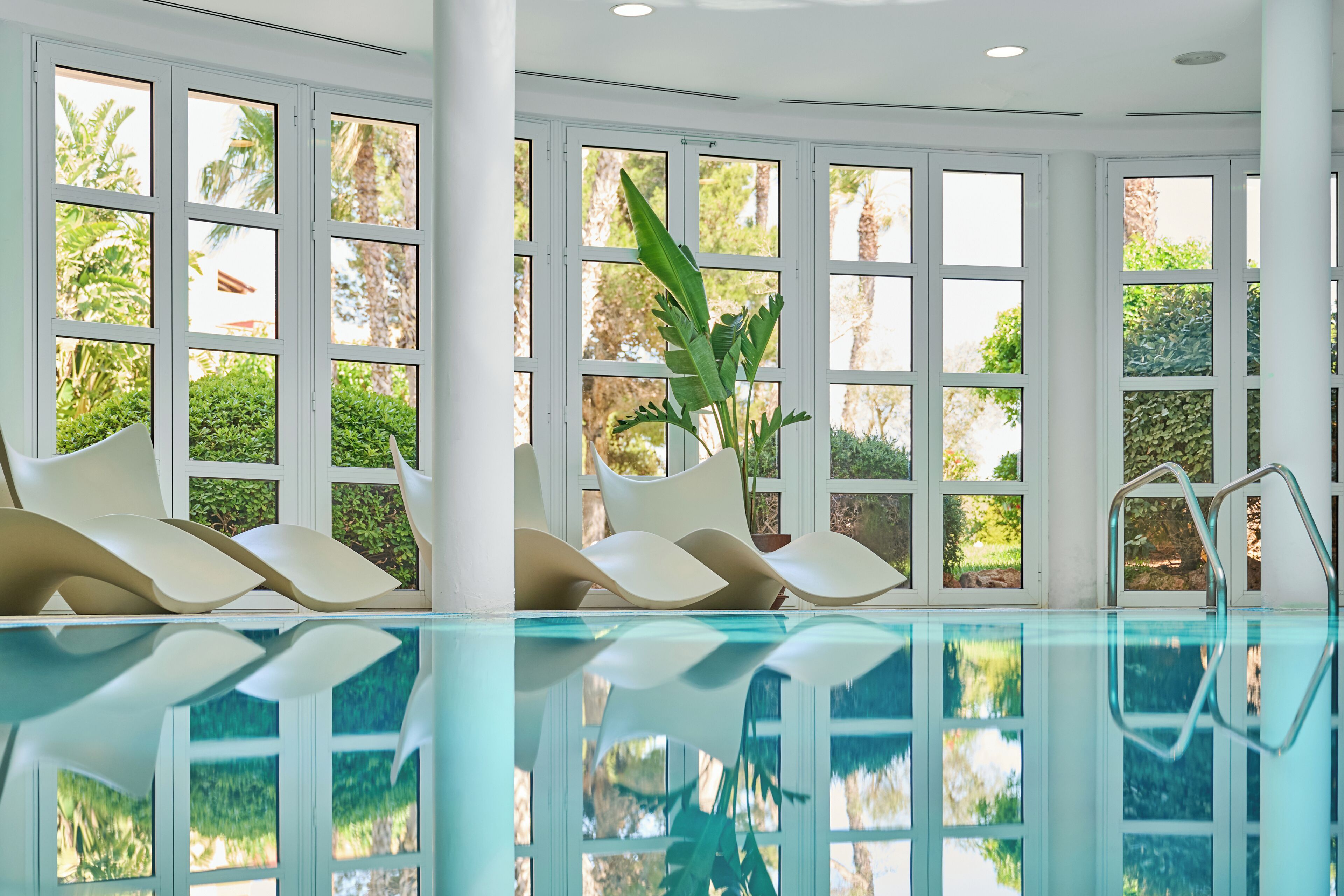 A pool area with modern chairs and a view of greenery through large windows.