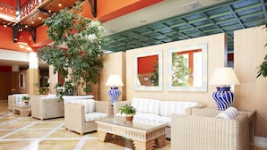A lobby with wicker furniture, a glass coffee table, and potted plants. - Grupotel Playa Club (Ciutadella de Menorca)