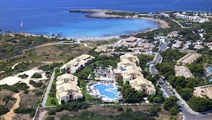 An aerial view of a coastal resort with multiple buildings, a swimming pool, and a beach area. - Grupotel Playa Club (Ciutadella de Menorca)