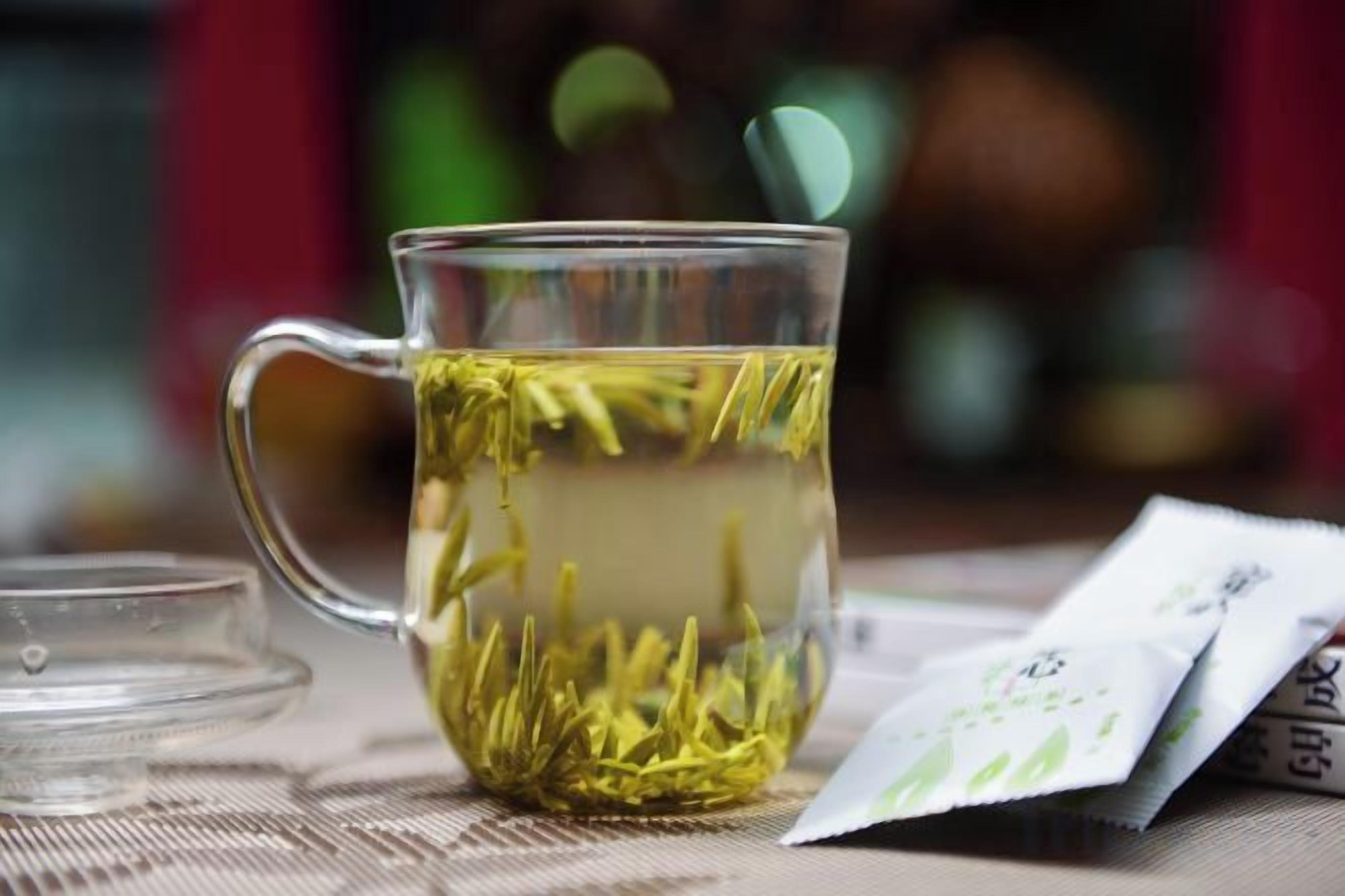 A clear glass mug filled with a yellowish liquid, possibly tea, with a tea bag visible inside.