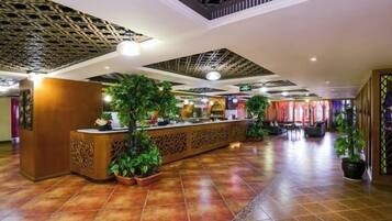 A hotel lobby with a reception desk, potted plants, and a patterned ceiling.
