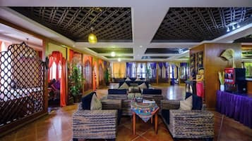 Un hall de hotel con sofás estampados, una mesa central y un techo decorativo.