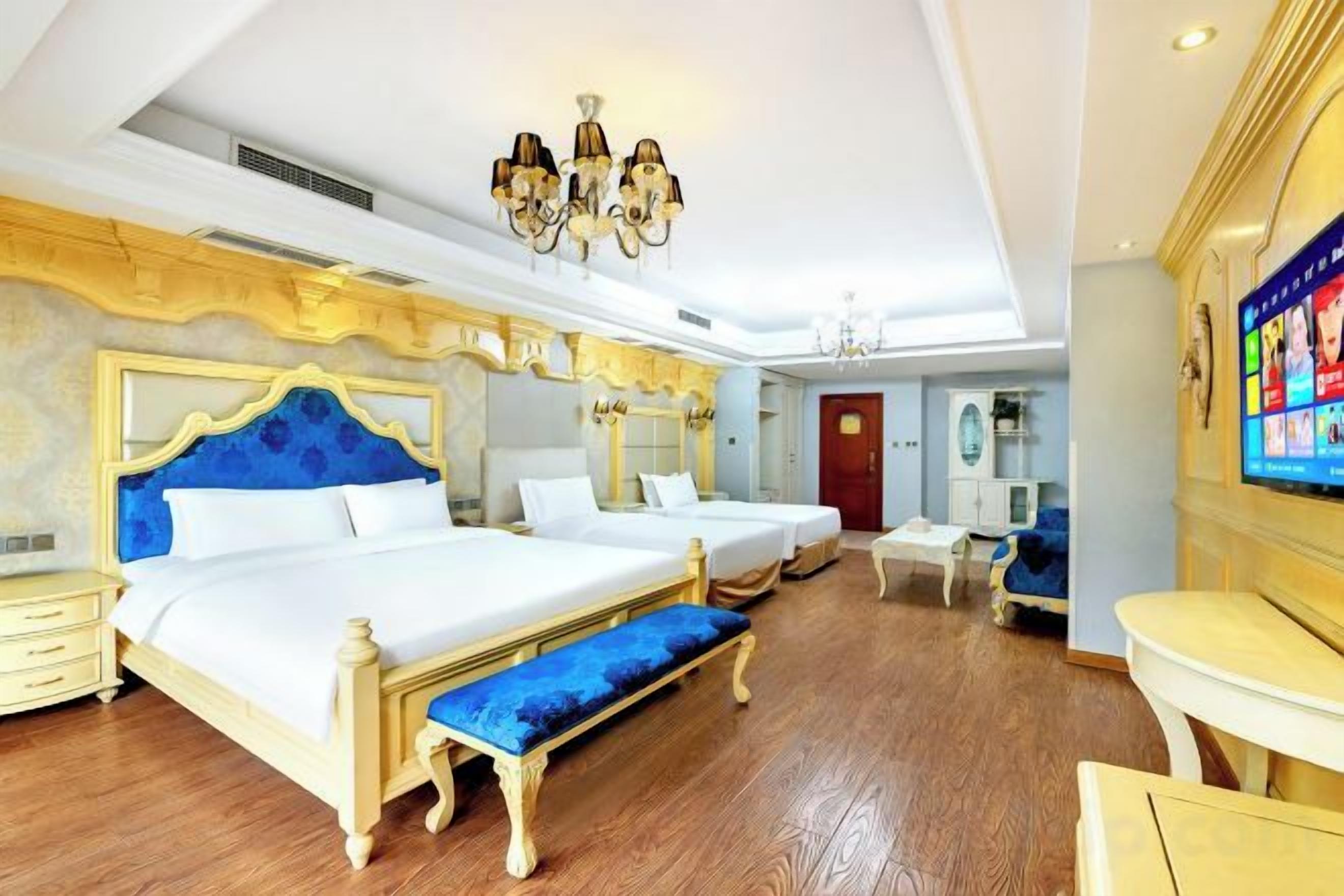 A hotel room with a large bed, a smaller bed, a bench, a desk, and a TV.