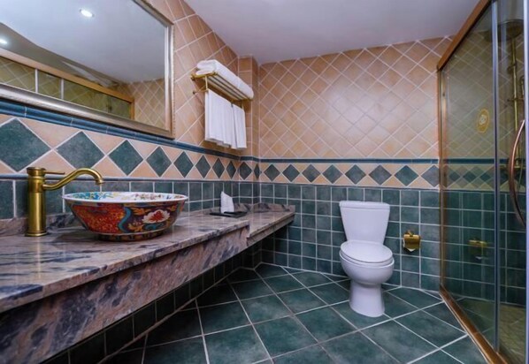 Une salle de bain dotée d’un comptoir en marbre, d’un lavabo décoratif en forme de bol, de toilettes blanches et d’une cabine de douche en verre.