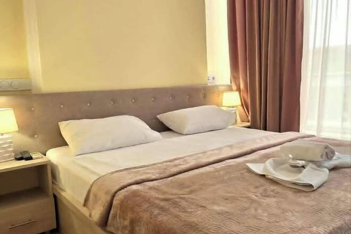 Una habitación de hotel con cama, mesitas de noche, una lámpara y una ventana con cortinas.