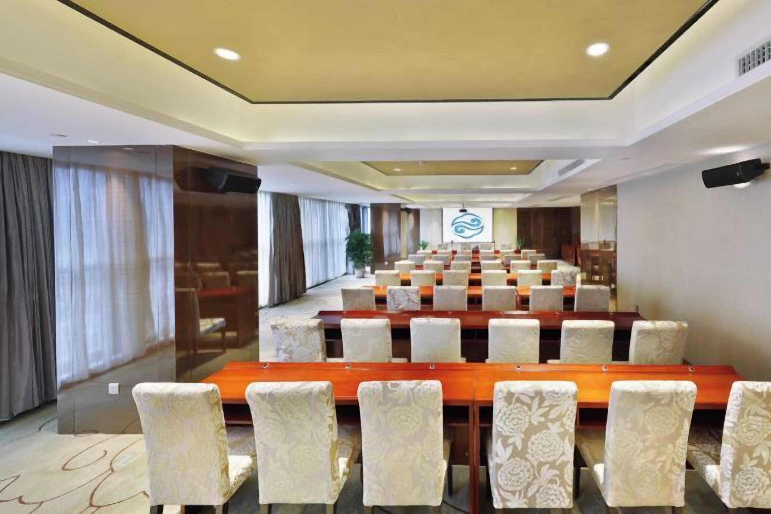 A conference room with rows of tables and chairs, a long table in the center, and a logo on the wall.
