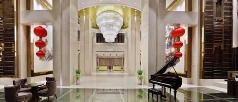 A spacious lobby with a grand piano, seating area, and a large chandelier.