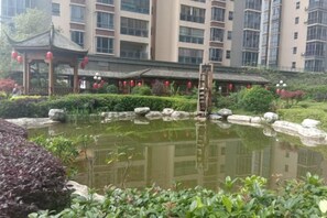 Un patio con un estanque, un pabellón tradicional y un edificio de varios pisos al fondo.