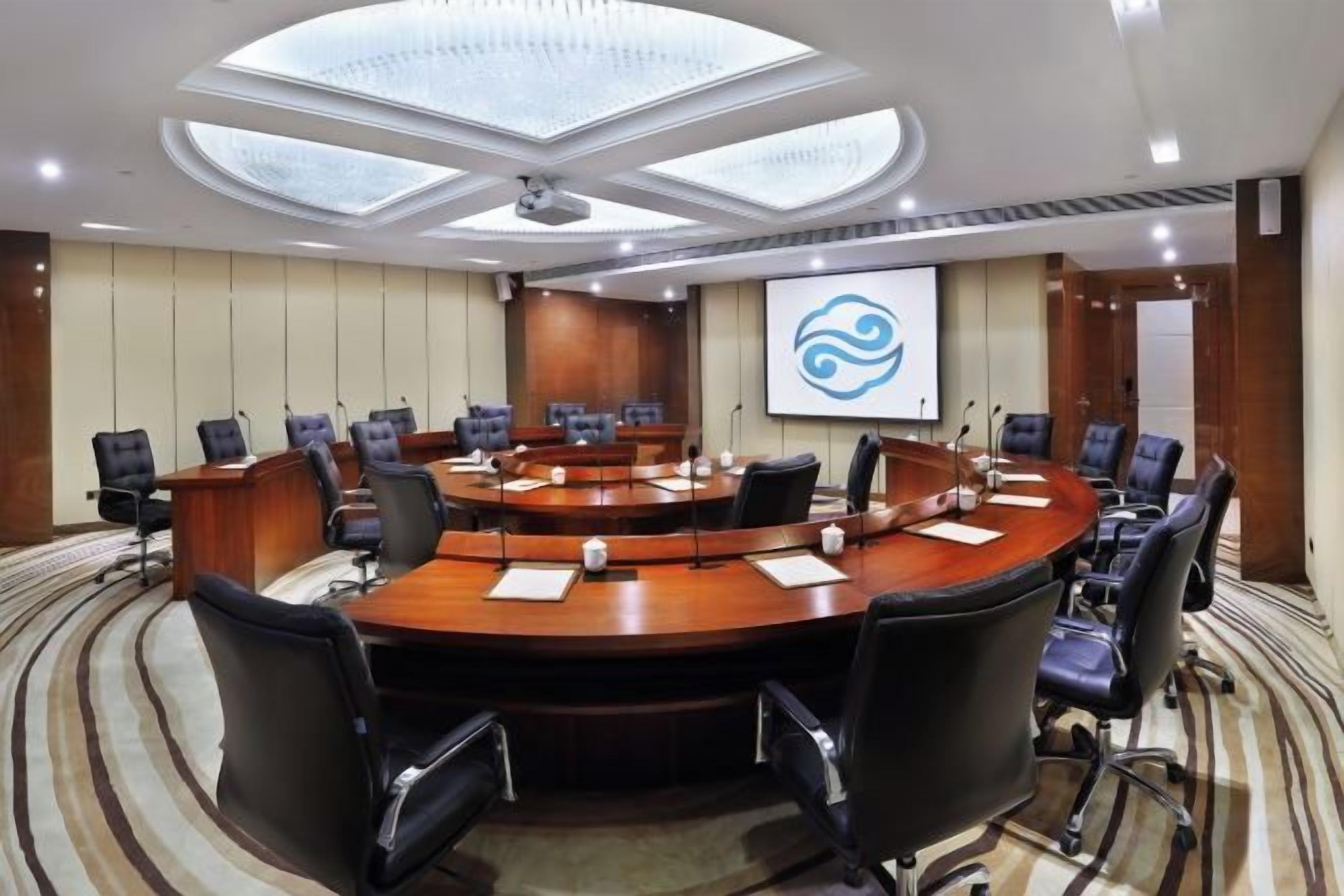 A conference room with a round table, multiple chairs, a projector screen, and a carpeted floor.