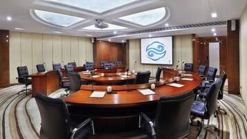 A conference room with a round table, multiple chairs, a projector screen, and a carpeted floor.
