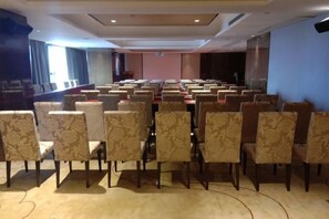 Uma sala de conferências com fileiras de cadeiras, um palco e uma tela grande.