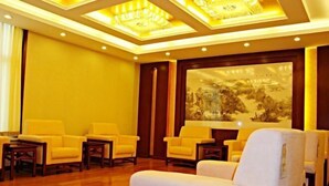 Een hotel lobby met een houten vloer, gele stoelen, een witte bank en een groot schilderij aan de muur.
