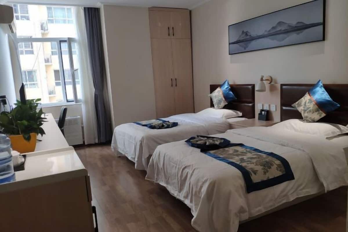 Une chambre d’hôtel avec deux lits, un bureau, une plante en pot, une armoire et un tableau au mur.