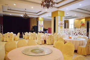 Een feestzaal met ronde tafels en stoelen, een podium en een decoratieve witte scheidingswand.