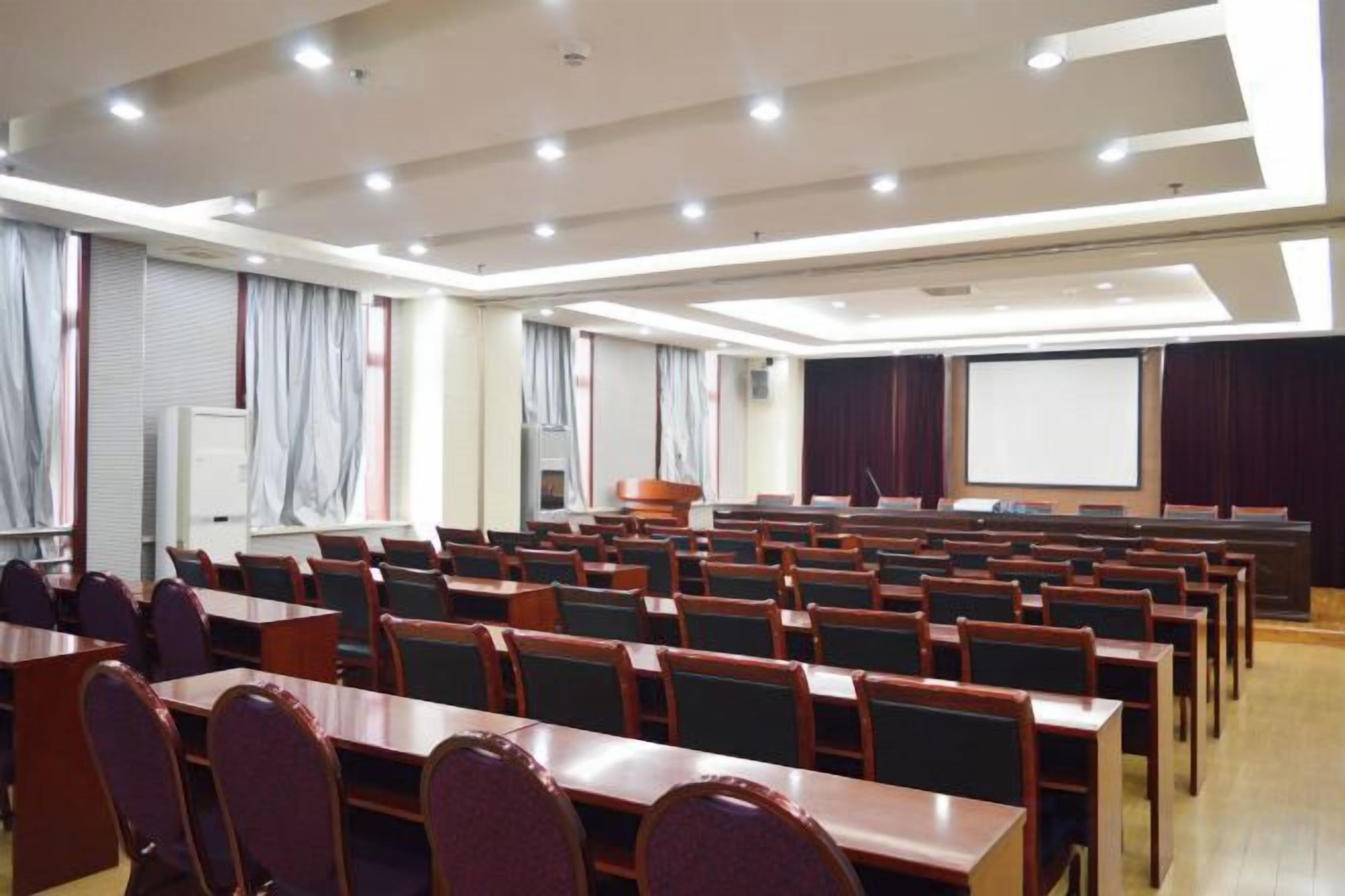 A conference room with rows of tables and chairs, a projector screen, and a whiteboard.