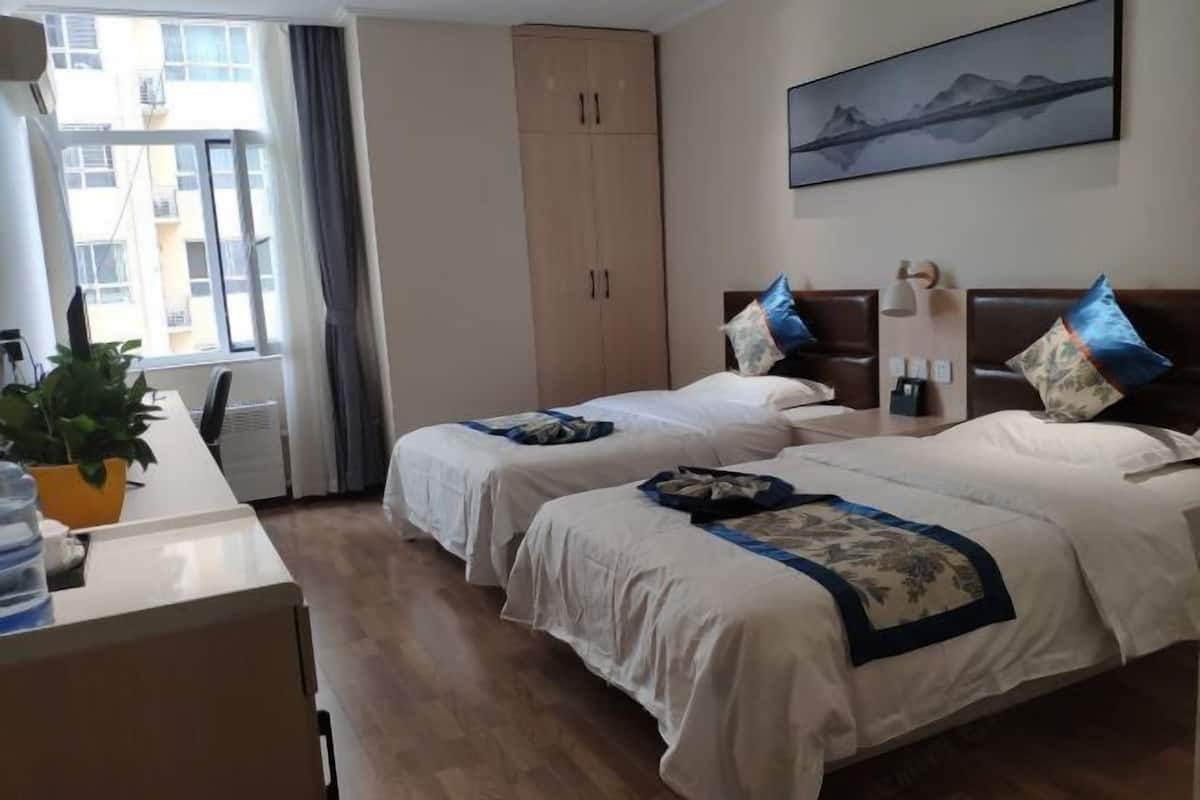 Une chambre d’hôtel avec deux lits, un bureau, une armoire, une fenêtre avec des rideaux et un tableau au mur.